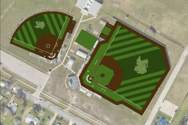 Aerial view of two adjacent baseball and softball fields with green, striped turf, brown infields, white baselines, and logos in center fields, surrounded by buildings, roads, and grassy areas.