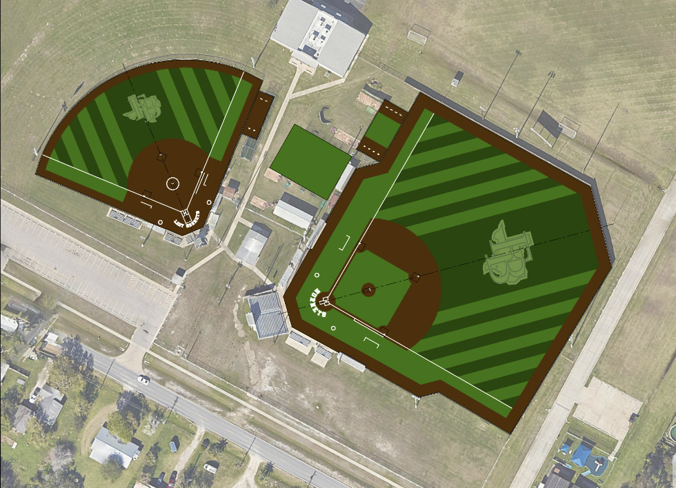 Aerial view of two adjacent baseball and softball fields with green, striped turf, brown infields, white baselines, and logos in center fields, surrounded by buildings, roads, and grassy areas.