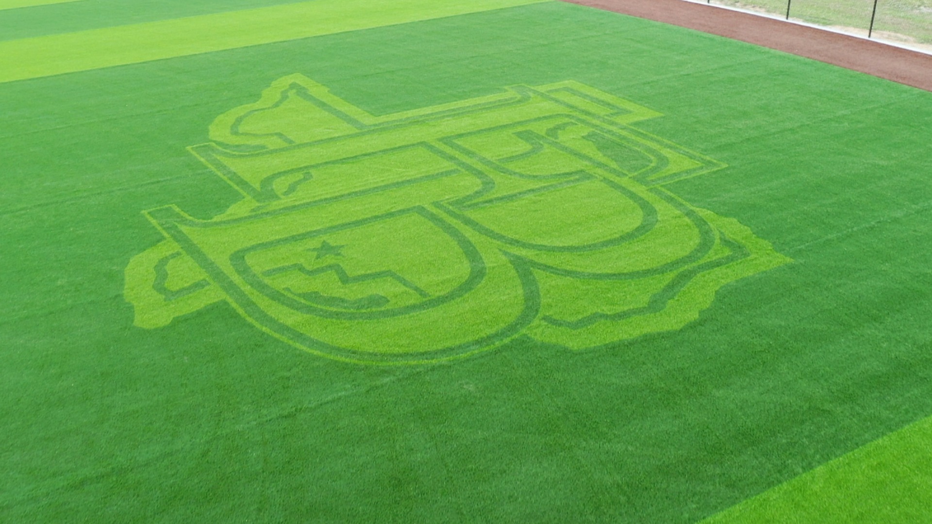 A baseball fields grassy outfield features an intricate design mowed into the turf, depicting a stylized logo with state and star shapes, surrounded by neatly trimmed, striped grass.