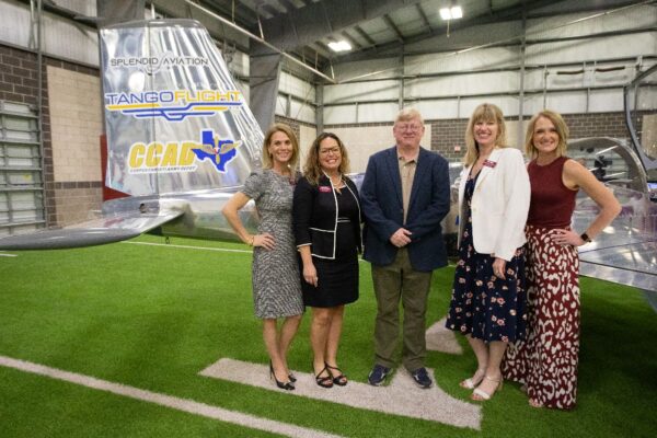 Five adults stand smiling in front of an aircraft tail inside a hangar. The tail displays Splendid Aviation, Tango Flight, and CCAD logos. Four women and one man are dressed in business-casual attire.