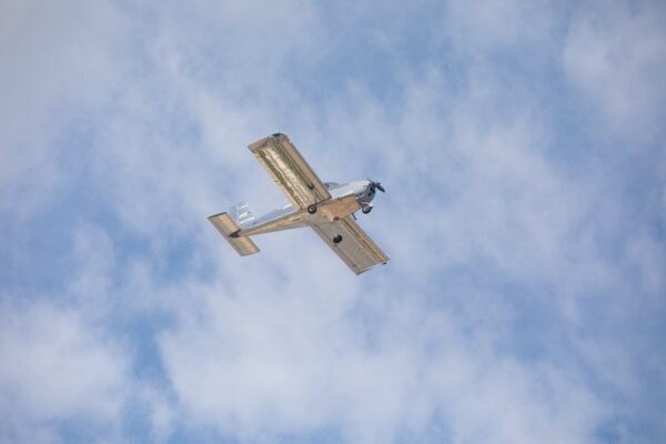 Flight Picture A small single-engine airplane is flying overhead against a backdrop of blue sky with scattered clouds.