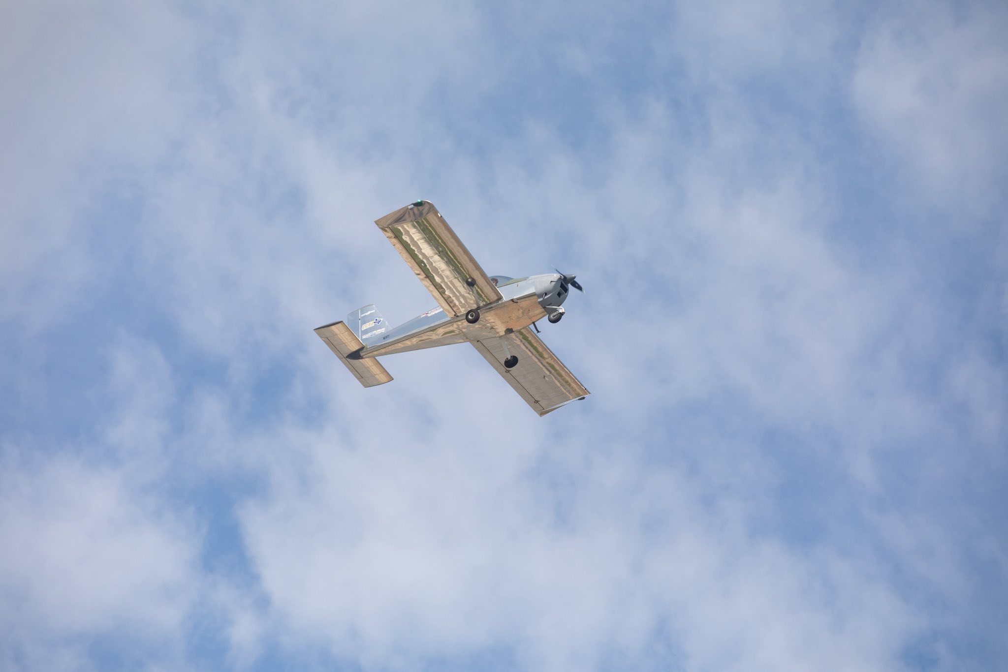 A small single-engine airplane is flying overhead against a backdrop of blue sky with scattered clouds.