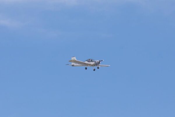 Hornet Aviation First Flight 7 A small single-engine airplane flying in a clear blue sky with a few wispy clouds.